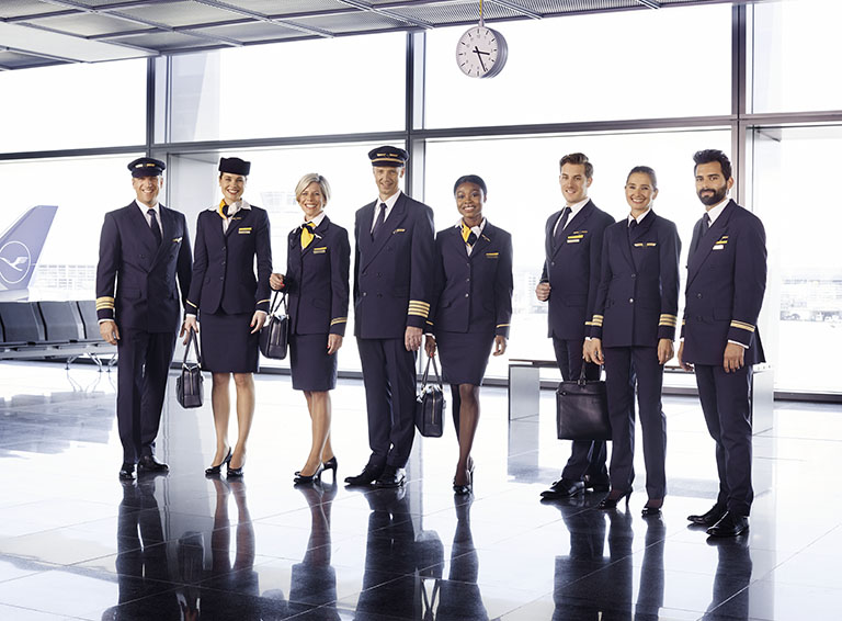 Drei Männer und vier Frauen verschiedener Herkunft in der dunkelblauen Lufthansa-Uniform